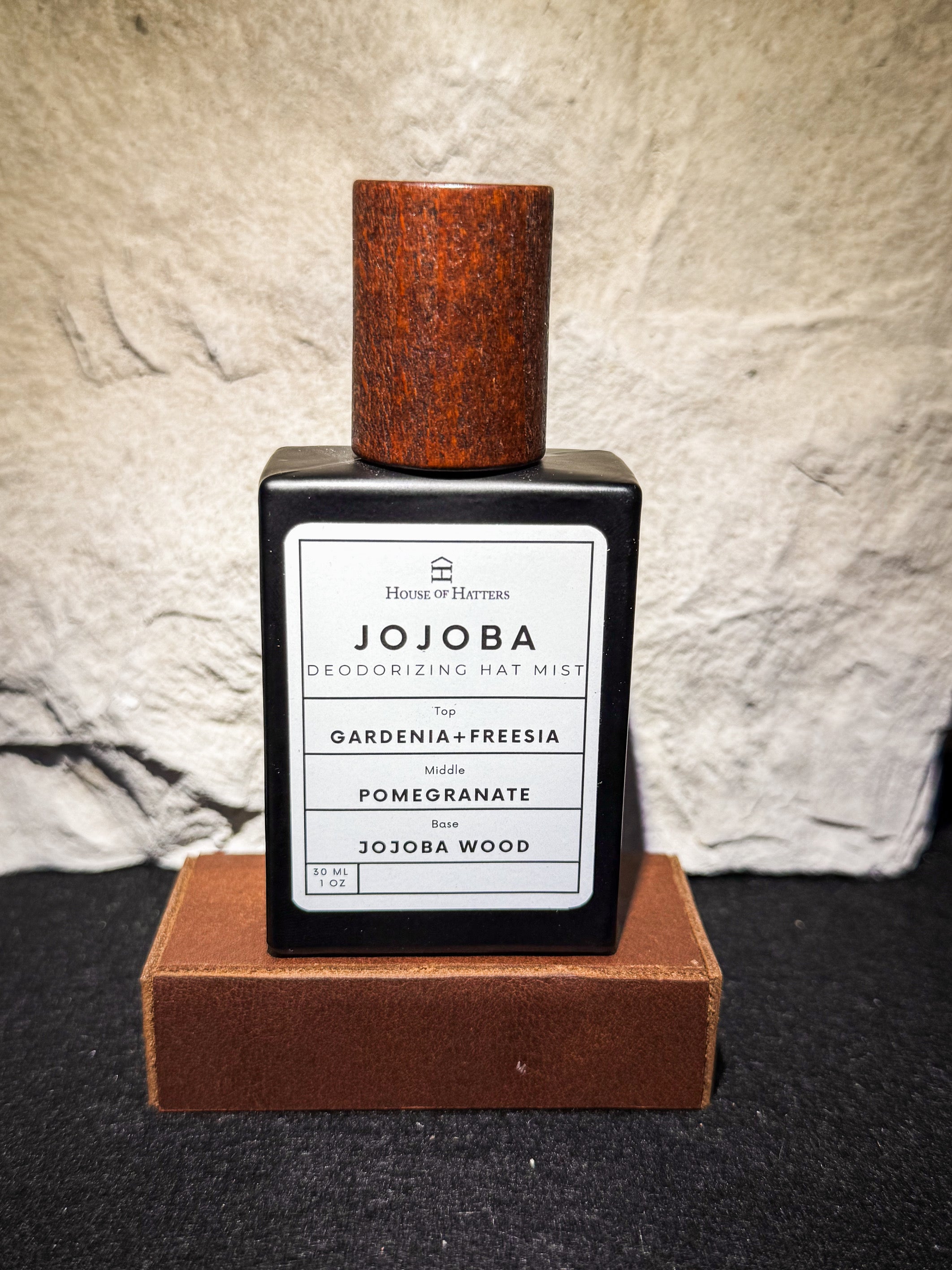 Jojoba deodorizing hat mist bottle with wooden cap on a textured surface