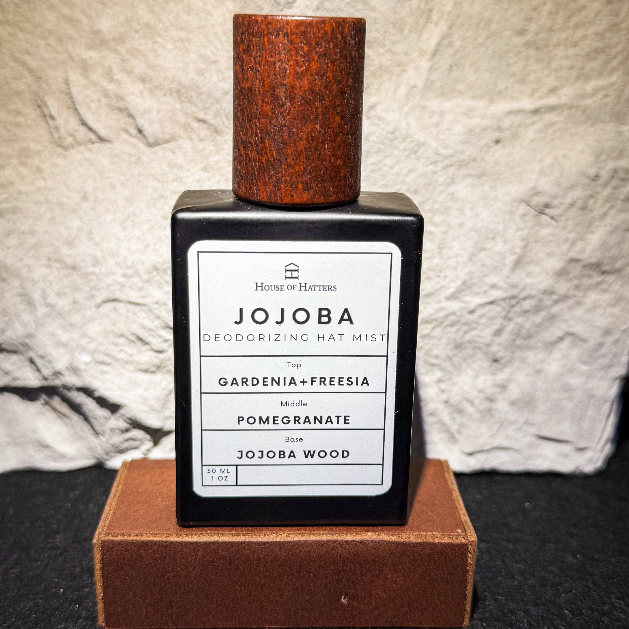 Jojoba deodorizing hat mist bottle with wooden cap on a textured surface