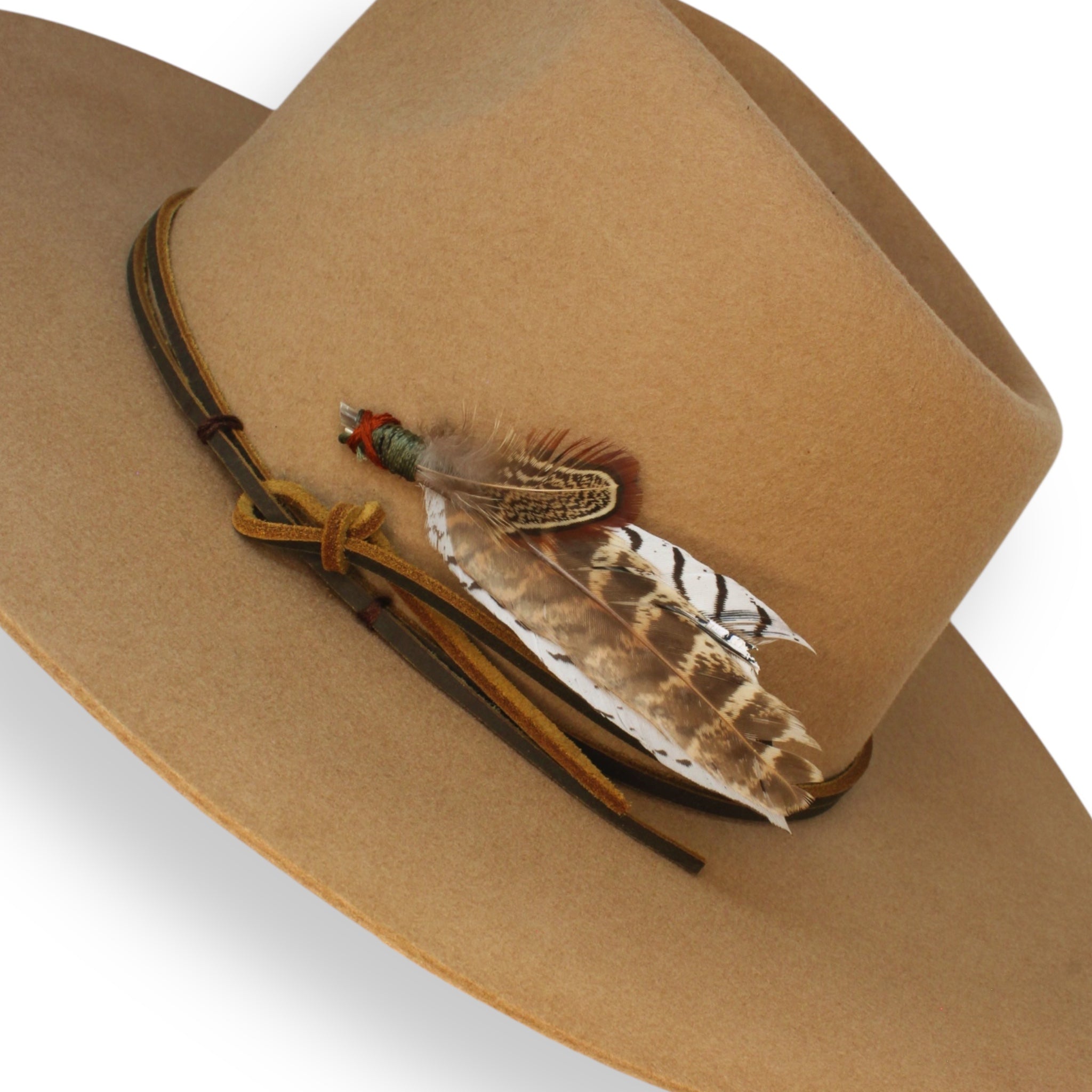 A detailed shot of a camel fedora with a handmade leather hat tie and a feather pin held in place by a dark red X stitch.