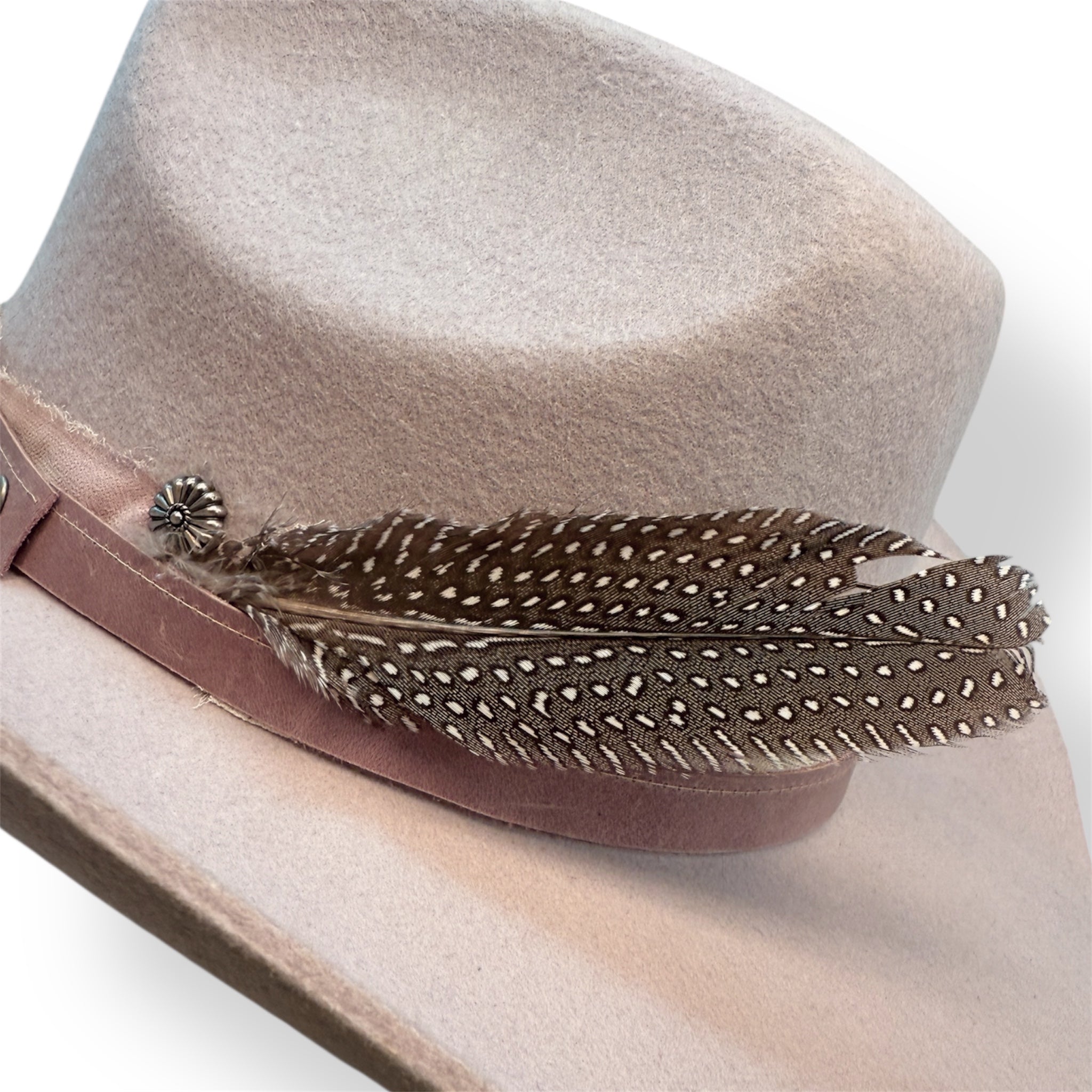 Detailed view of the lavender cowboy hat with a pink gray leather band, distressed ribbon, silver flower concho, and a large spotted feather.