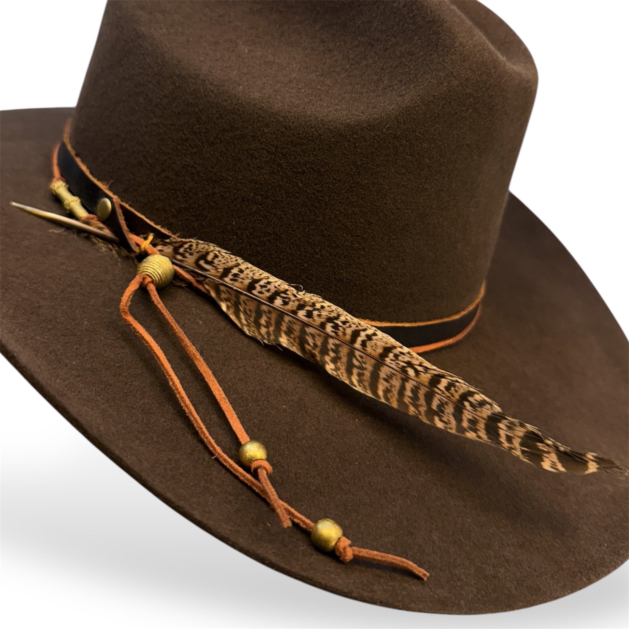 Detailed view of the chocolate brown cowboy hat with a dark leather hat band, burnt orange hat tie with brass beads, and a large ringneck pheasant tail feather.