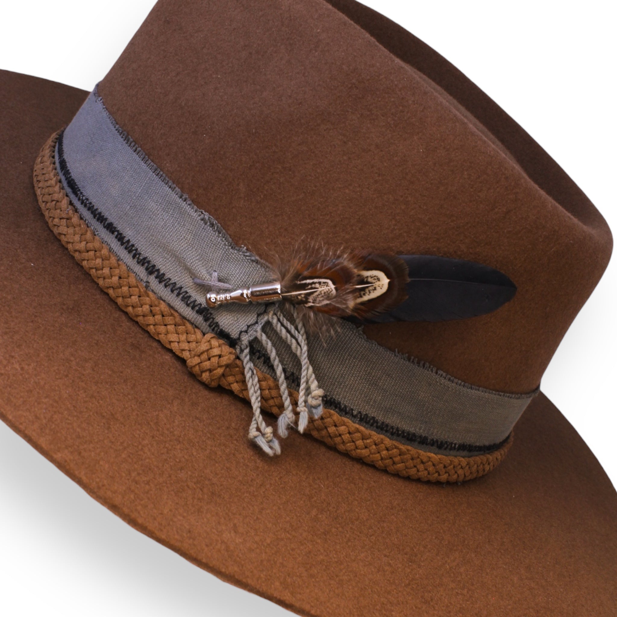 Detailed shot of the felt hat. The textile band is gray and has braided ropes from the end. Three feathers are nestled into the silver feather holder.