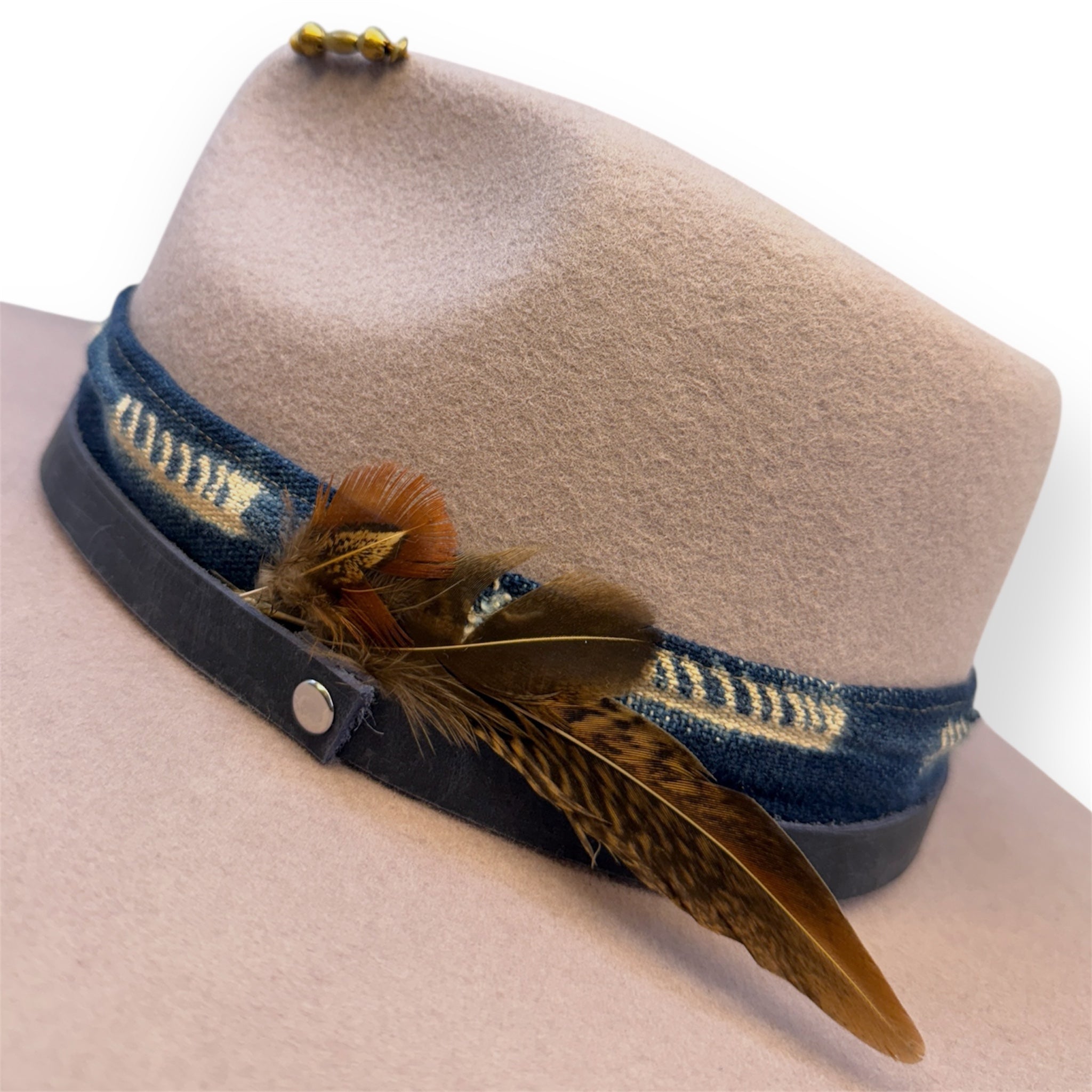 A detailed shot of a lavender felt fedora hat with a feather pin, blue hat bands, and five brass beads on the crown.