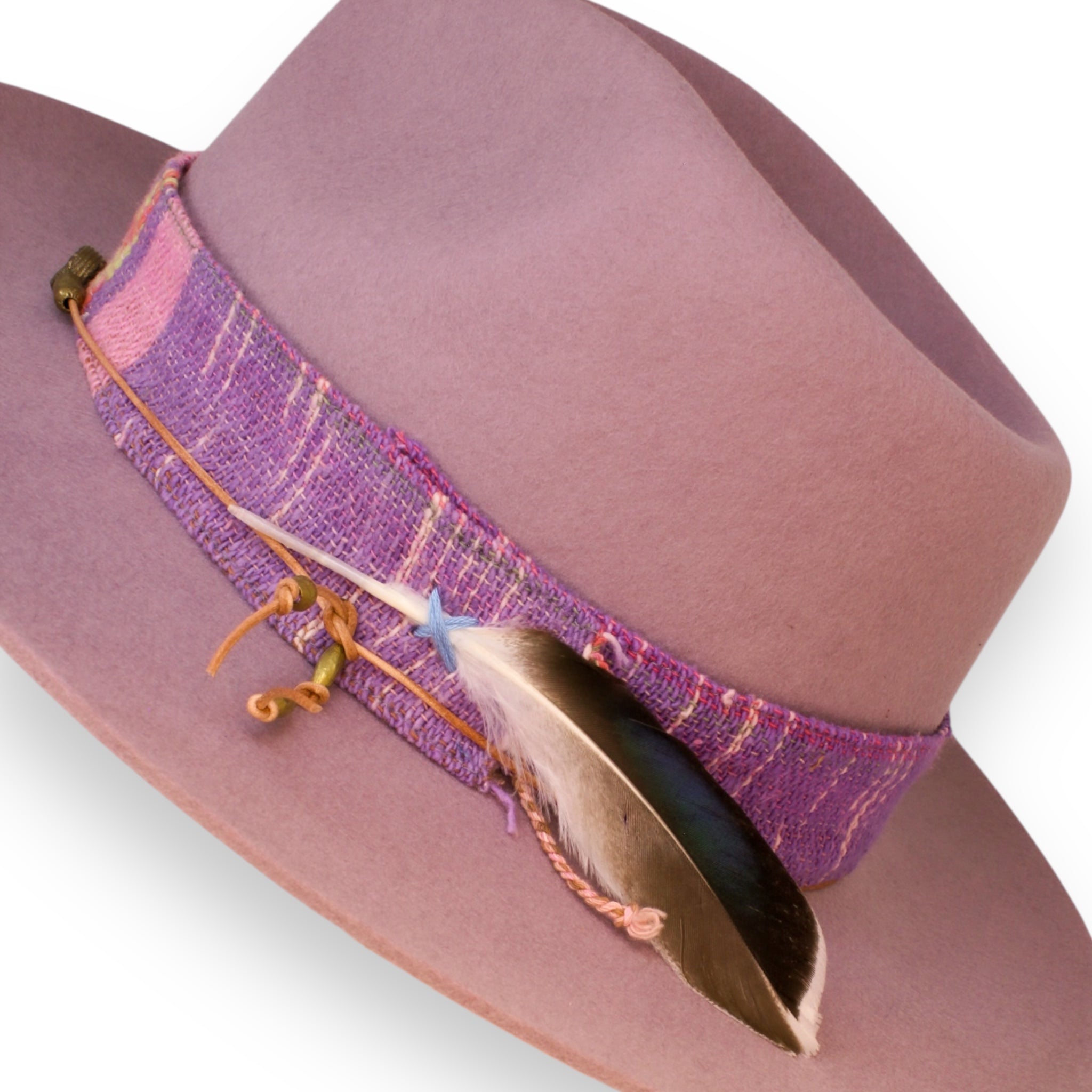 A detailed shot of the pale plum hat with a textile band, an orange and brass hat tie, and a white and brown feather with a slight blue sheen.