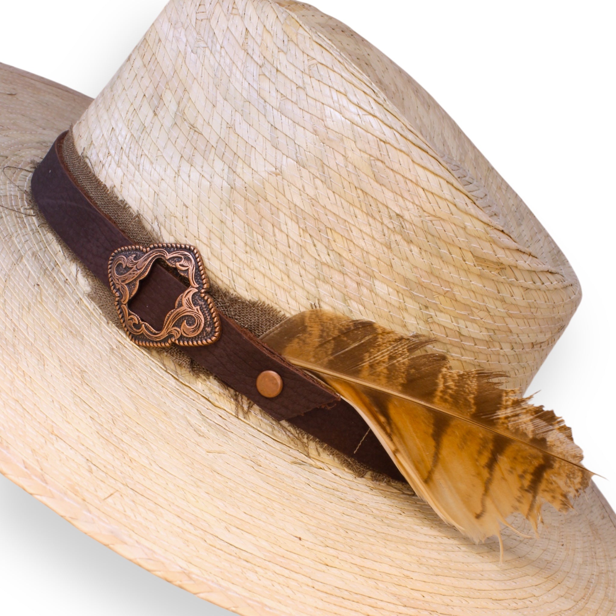 A detailed shot of the natural palm fedora showing off the intricacies of the copper buckle on the dark brown leather hat band, the distressed ribbon, and the large feather.