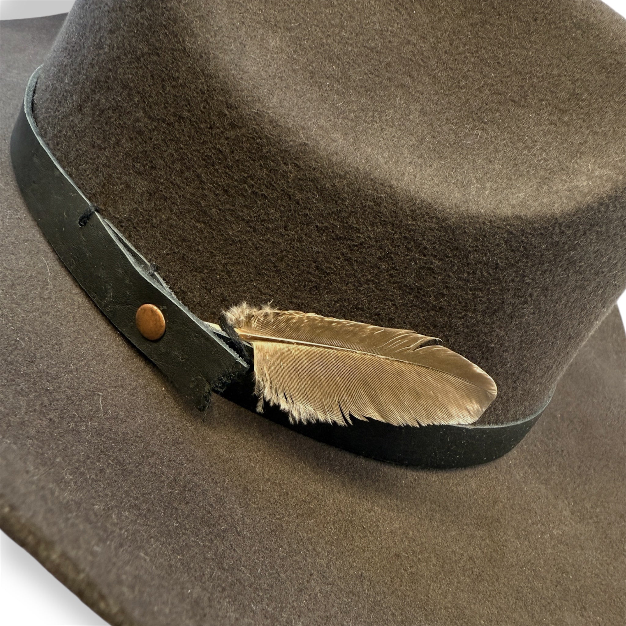 Detailed view of the gray cowboy hat with a black leather hat band and a small gray feather.
