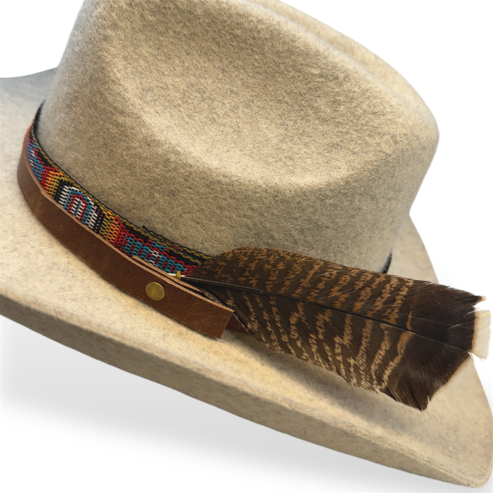 Detailed view of the multicolored light tan and gray hat with a premium leather hat band, indigenous patterned ribbon, and a large turkey feather.