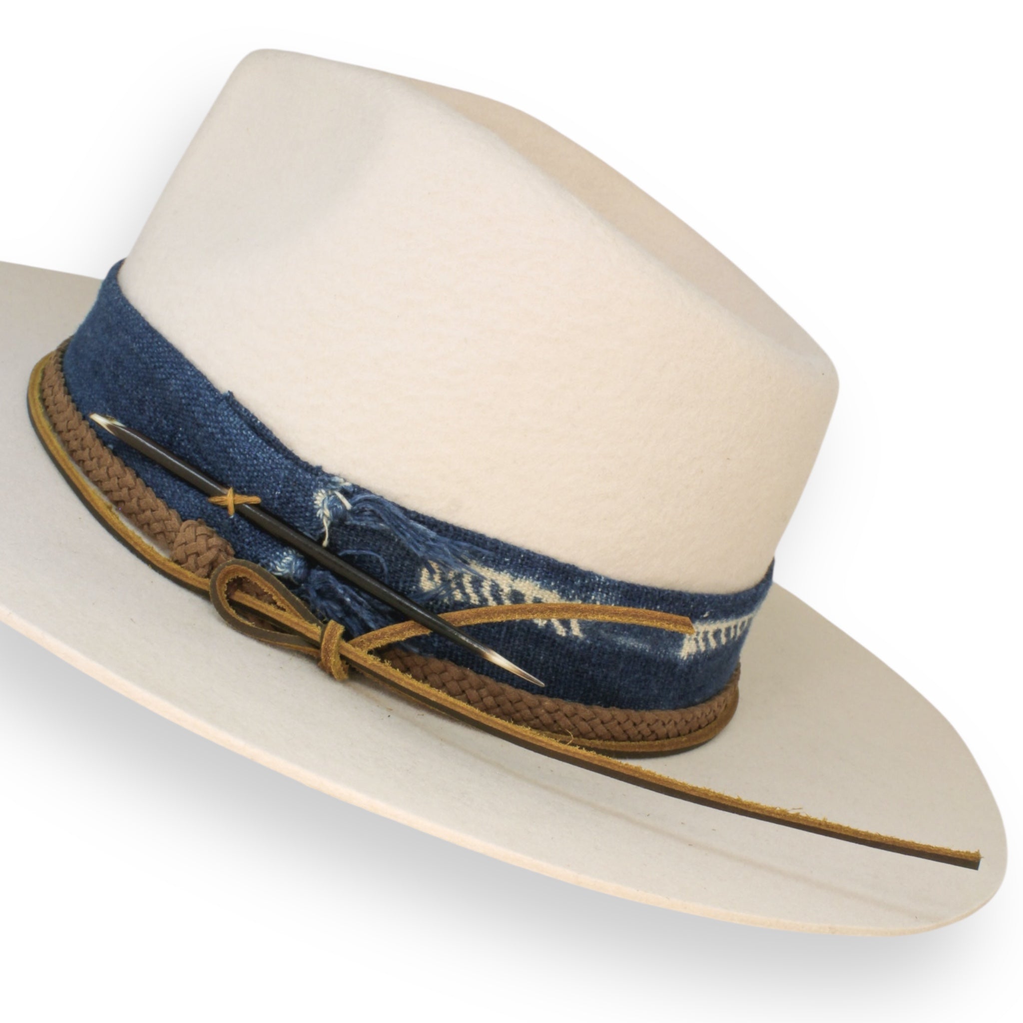 A detailed shot of the white broken teardrop fedora with blue textile, a braided cord band, a handmade leather hat tie, and a short porcupine quill.